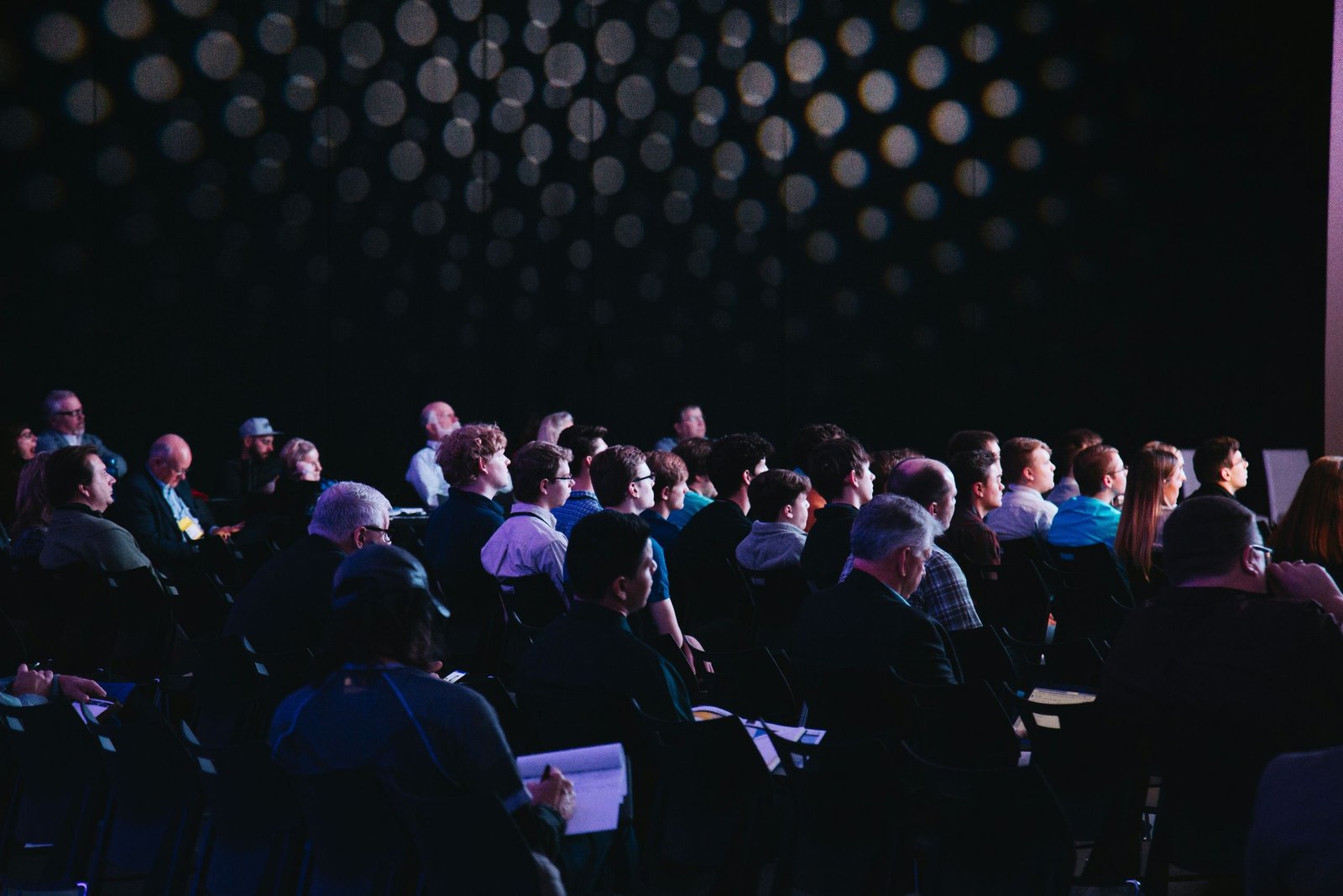 A dark auditorium filled with attendees watching a presentation