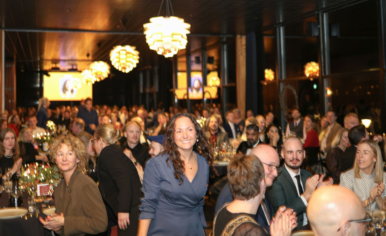 Guests laughing and talking at a long dinner under hanging lanterns