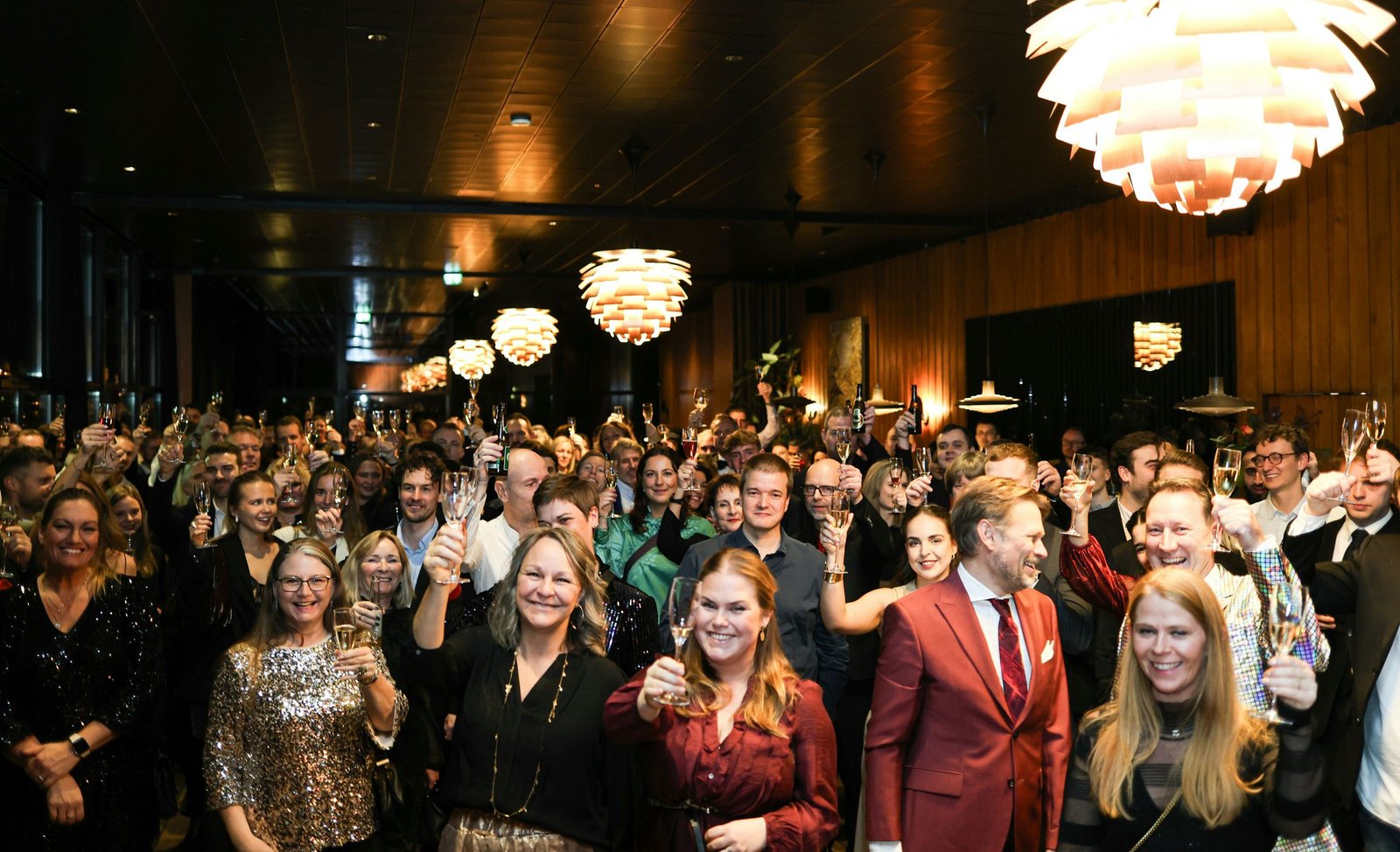 A cheering crowd raising their glasses under warm pendant lights